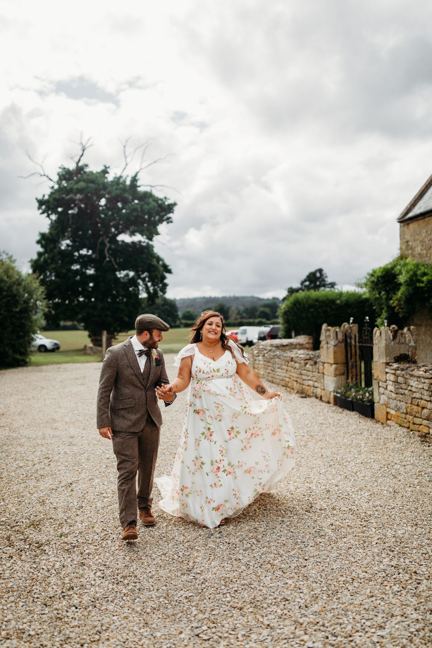 A couple walking and laughing along a gravel path by a stone wall countryside venue.