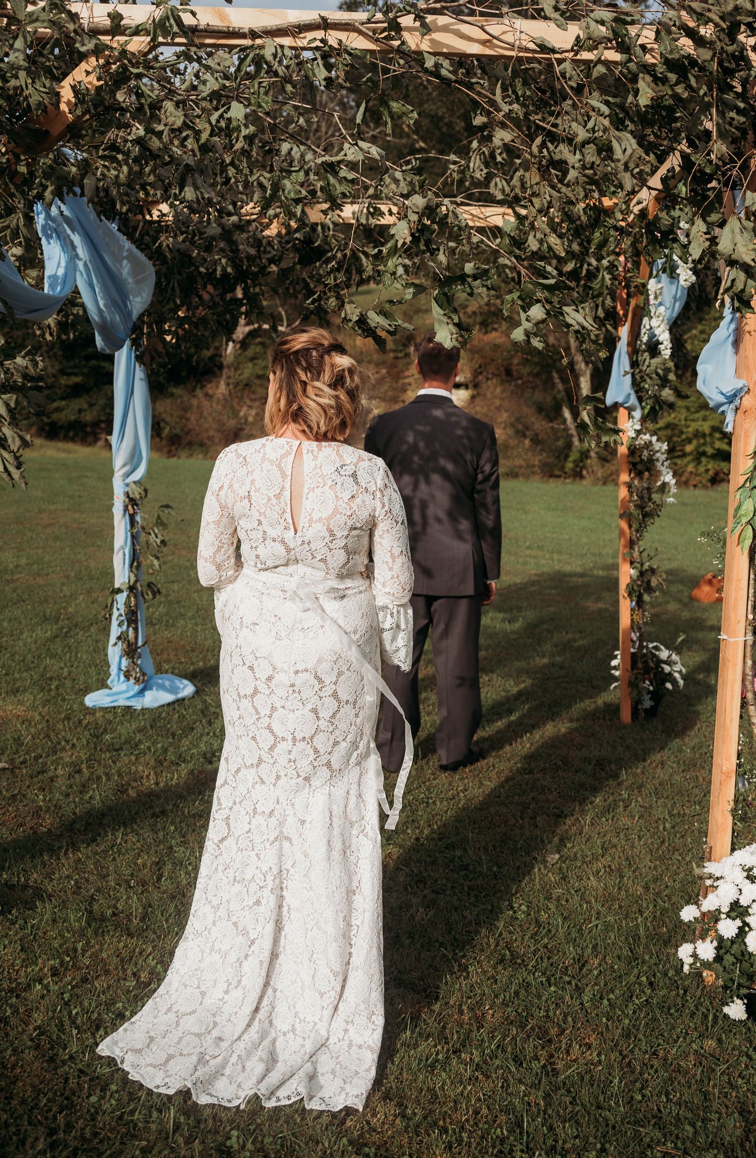 An elegant white lace wedding dress photographed against a rustic outdoor backdrop with blue fabric decor.
