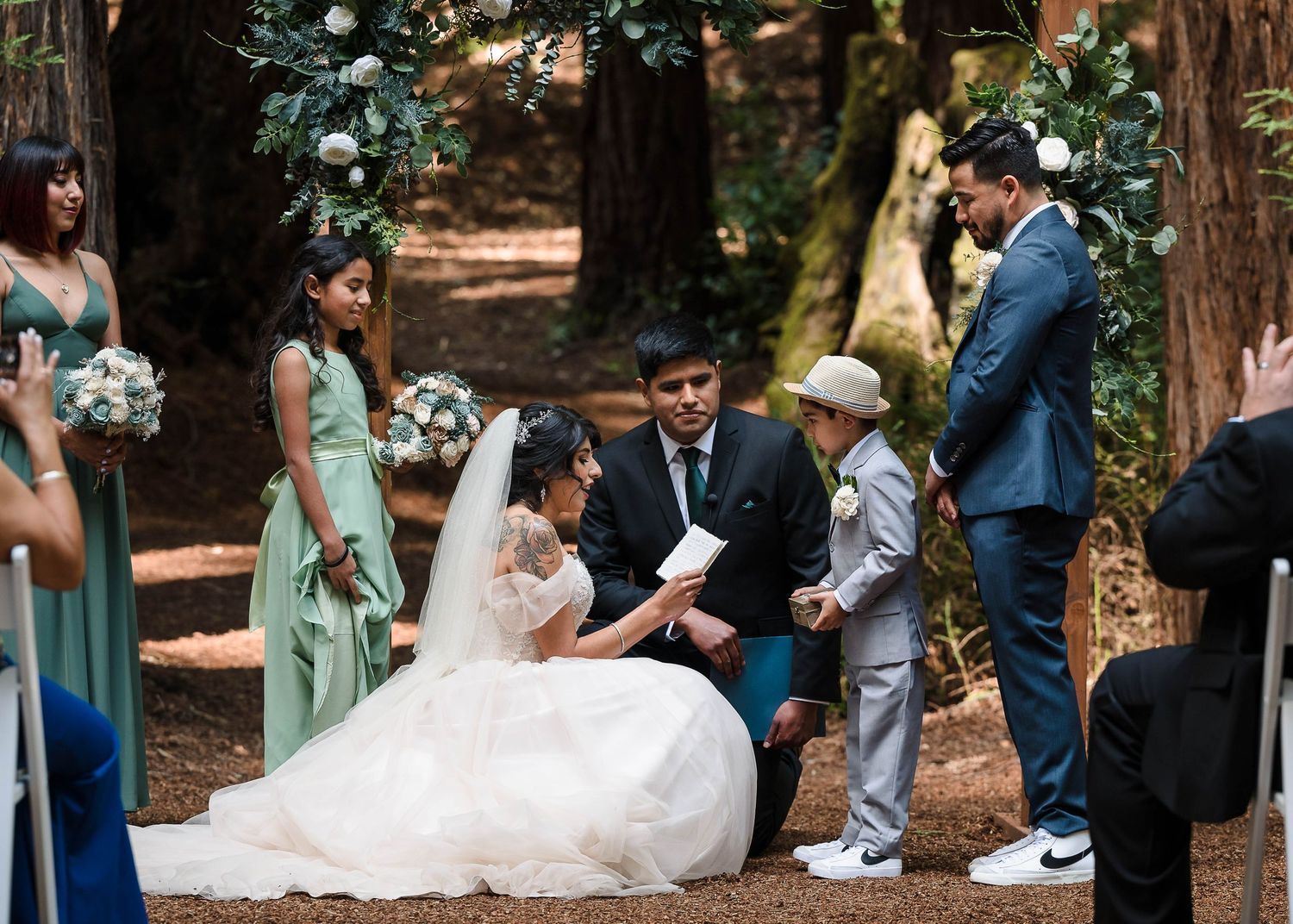 Wedding ceremony in a redwood forest with bridesmaids in mint green dresses gathering around the couple.