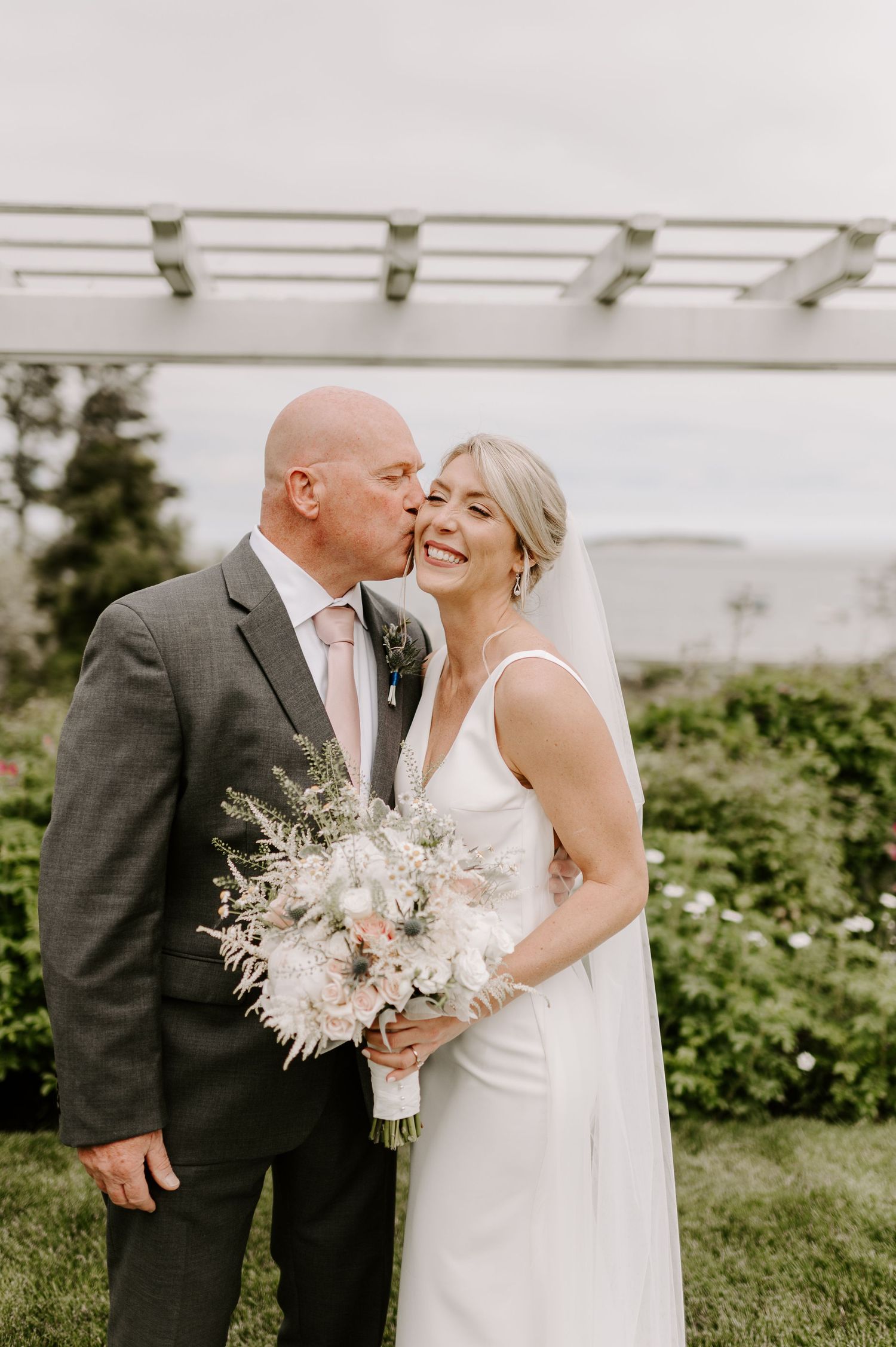 Wedding couple embraces and shares tender moment while holding delicate white bouquet.