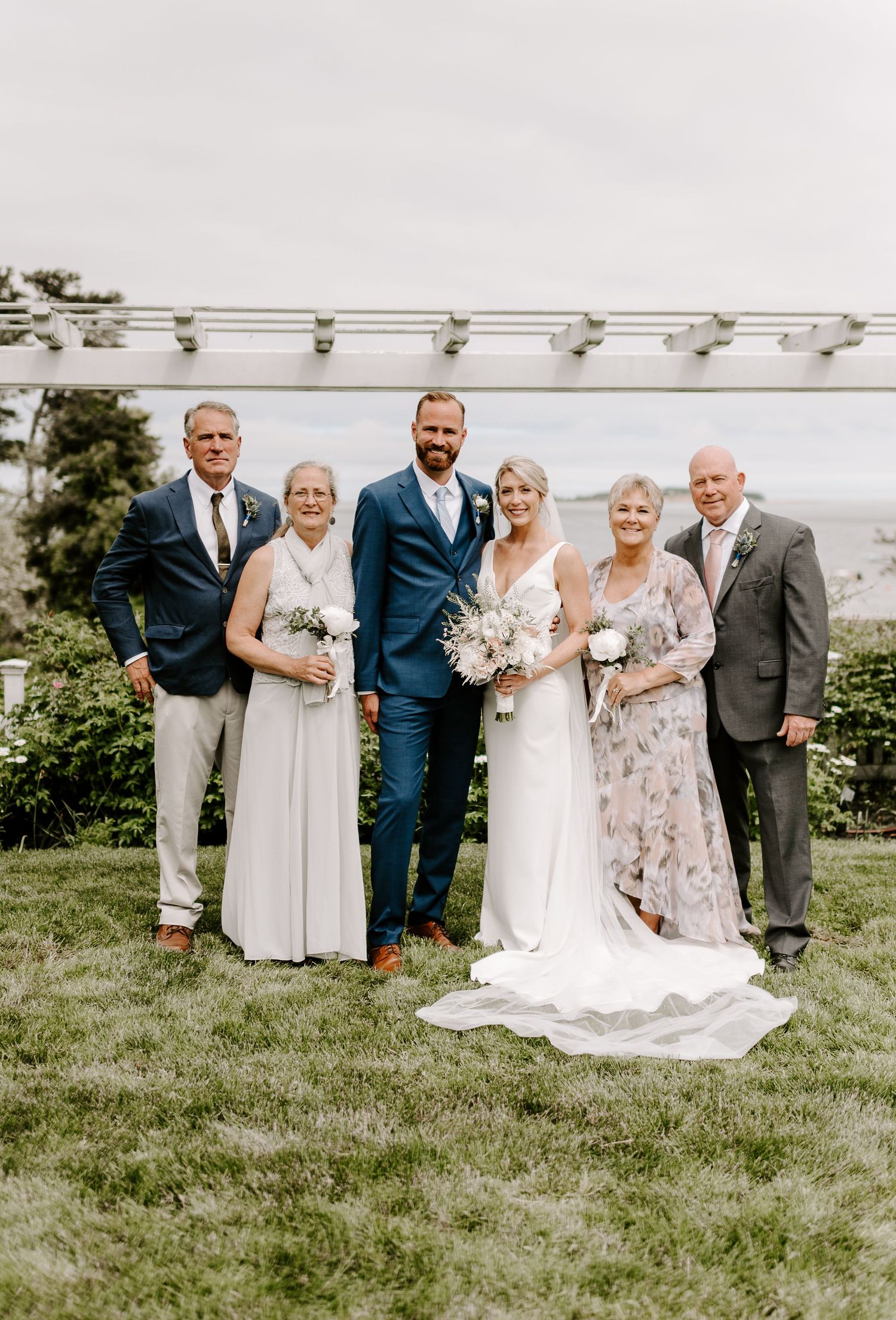Wedding party poses together on grassy hillside with ocean view in background.