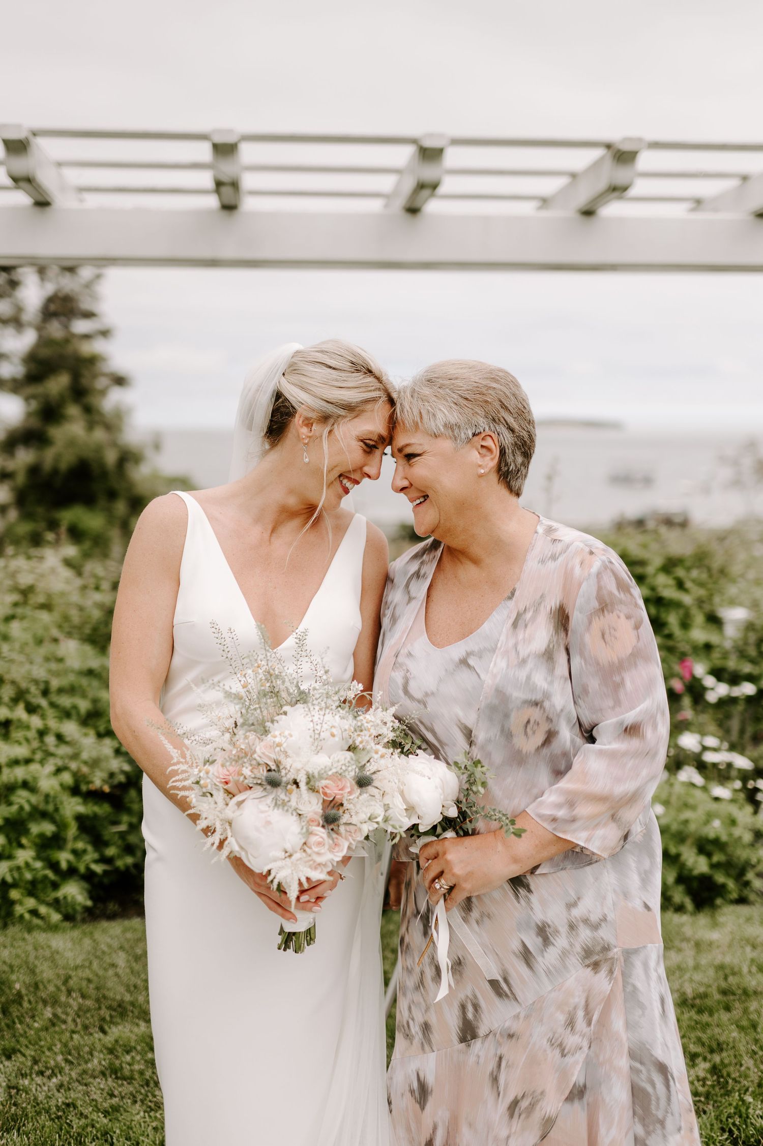 Two people share an intimate moment while holding white floral bouquets outdoors.
