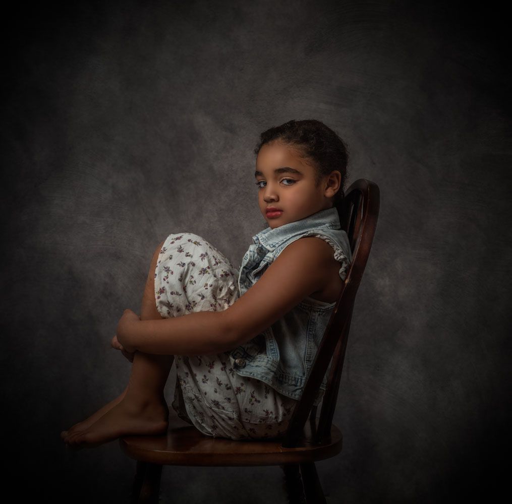Fine Art Portrait. Girl Sitting on a chair facing the camera. She has her knees pulled to her chest