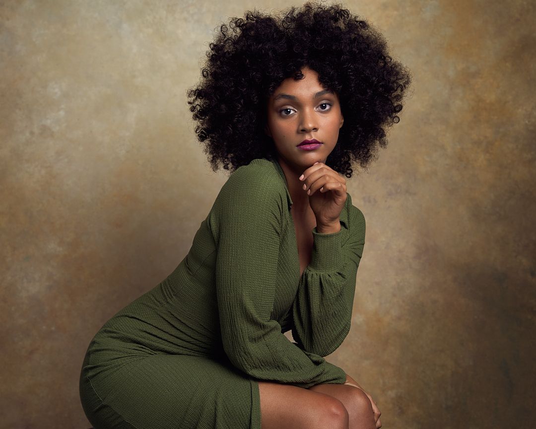 Young woman with natural afro hair in olive green dress posing gracefully.