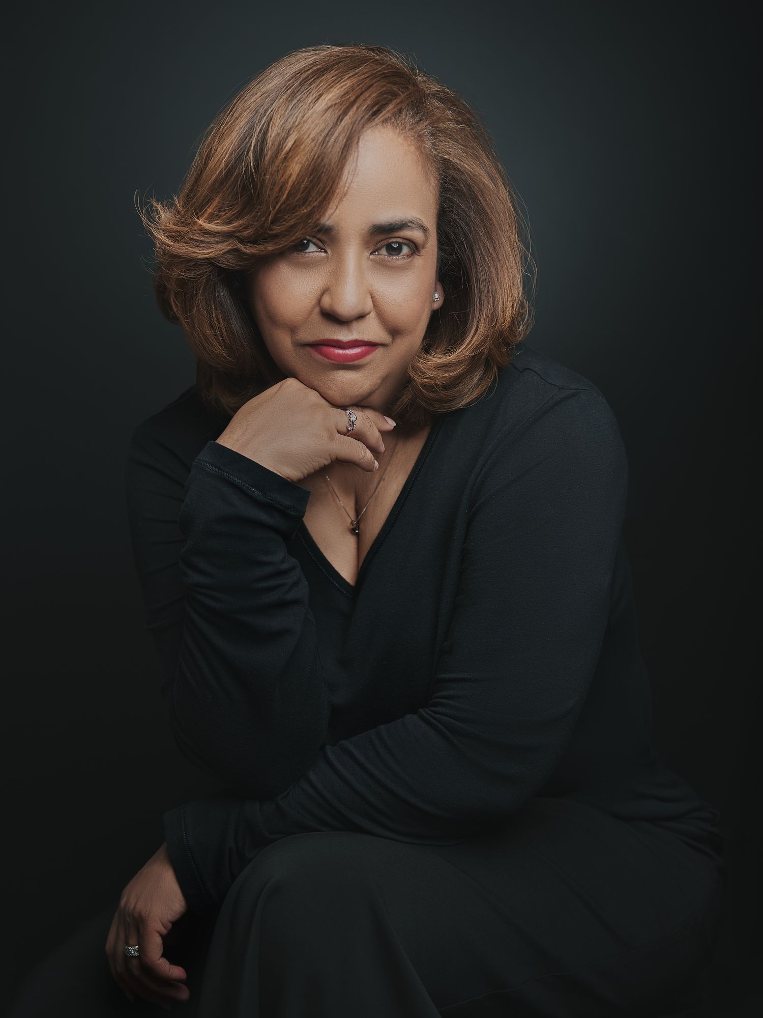 Professional portrait of a woman in black top with warm brown hair against dark background.