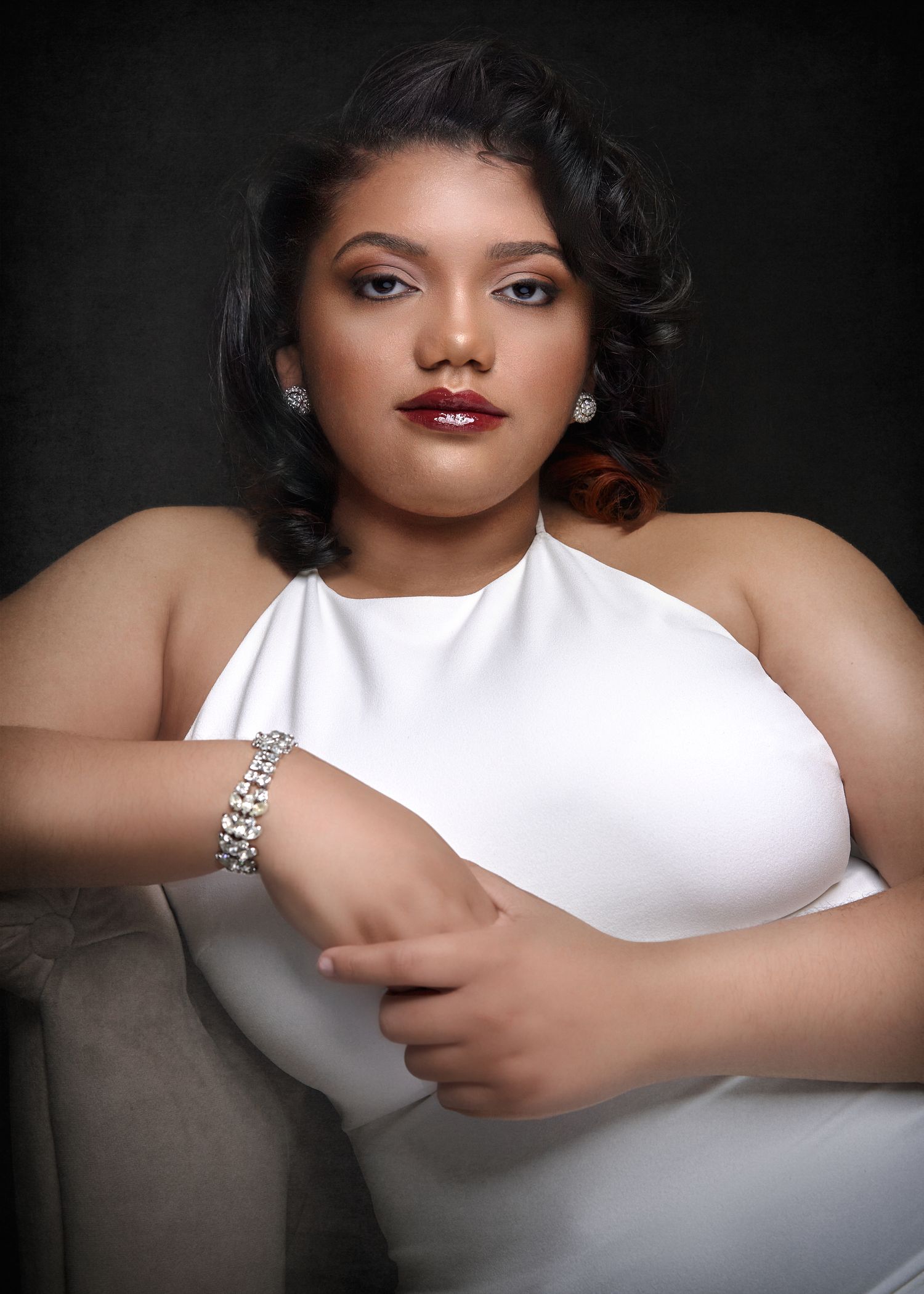 Glamorous woman in white halter dress with diamond jewelry posing in studio portrait.