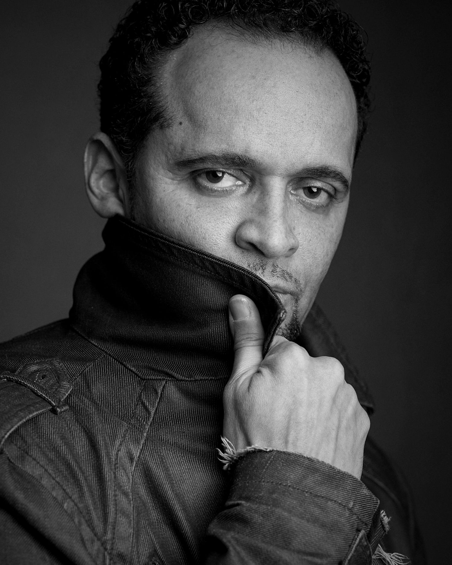 Black and white portrait of man in turtleneck jacket with thoughtful expression.
