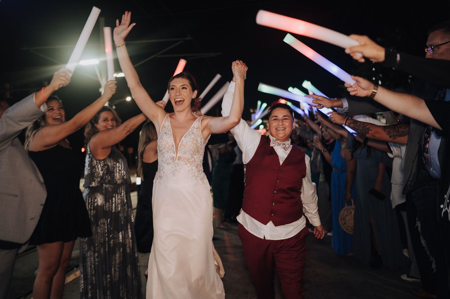 Wedding celebration with glow sticks creating a light tunnel for dancing couple.