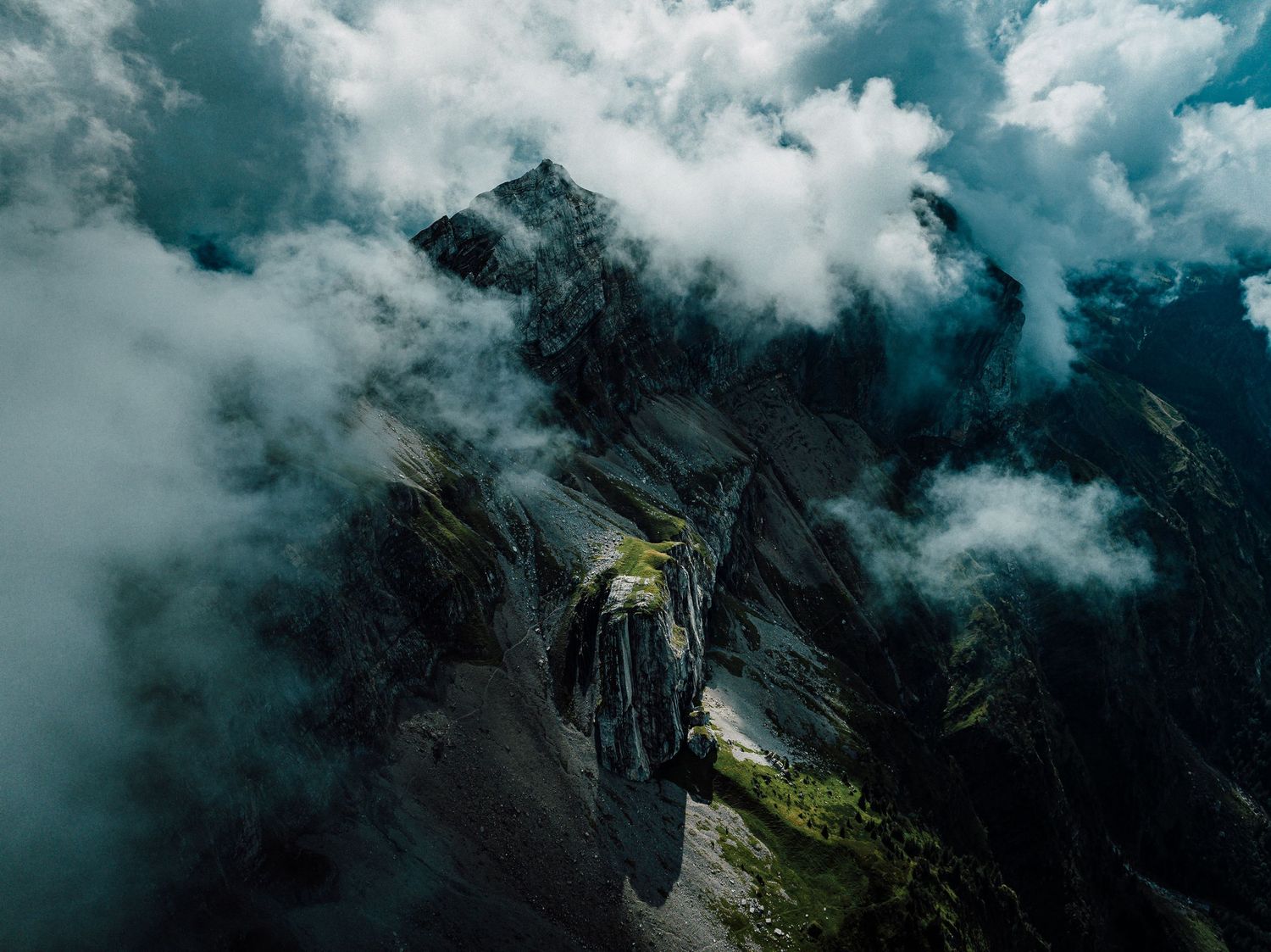 Dramatic aerial view of misty mountain peaks and winding road through clouds.
