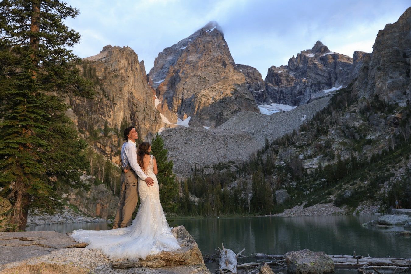 Wedding couple walking through mountain landscape with towering peaks and alpine lake views.