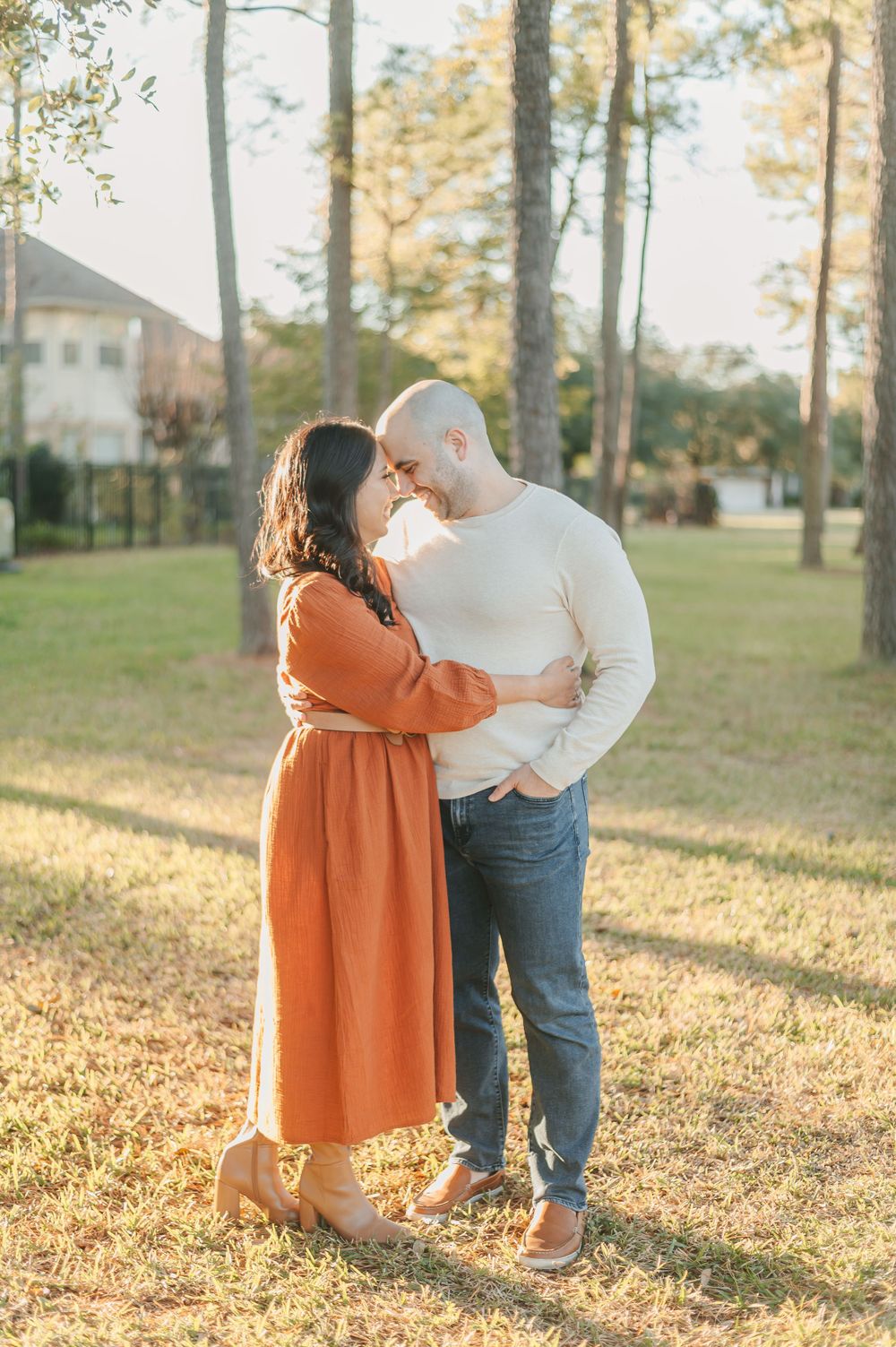 A romantic couple embracing in a park setting with golden afternoon light.