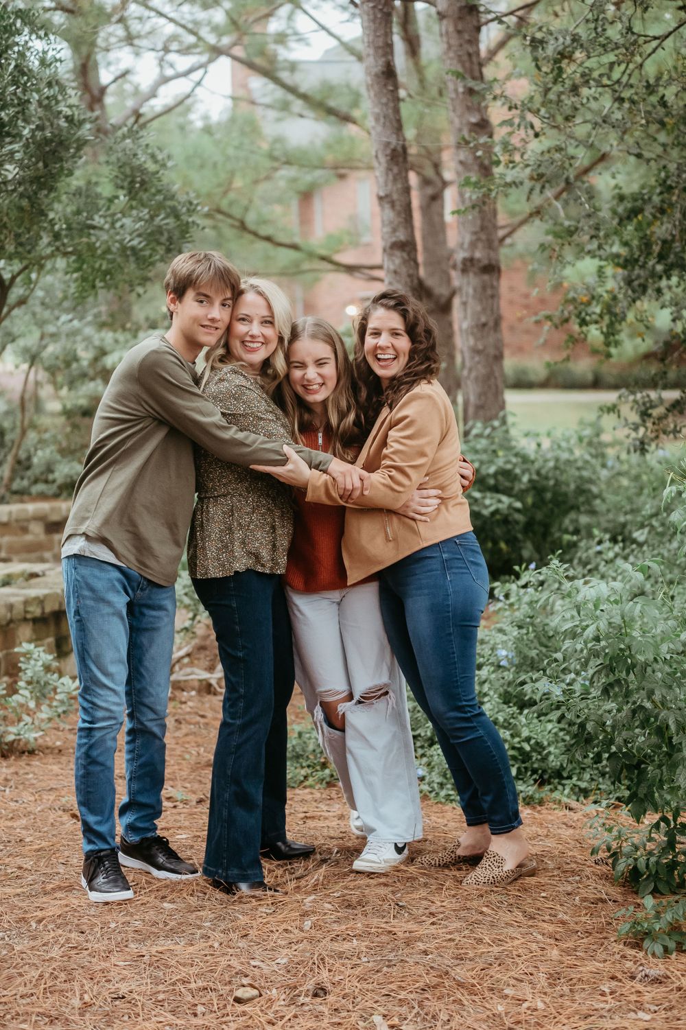 A group embraces together outdoors on a pine needle covered path surrounded by trees.