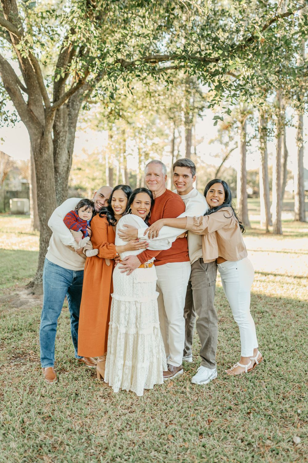 Family group photo outdoors with coordinated autumn-colored outfits under a large tree.
