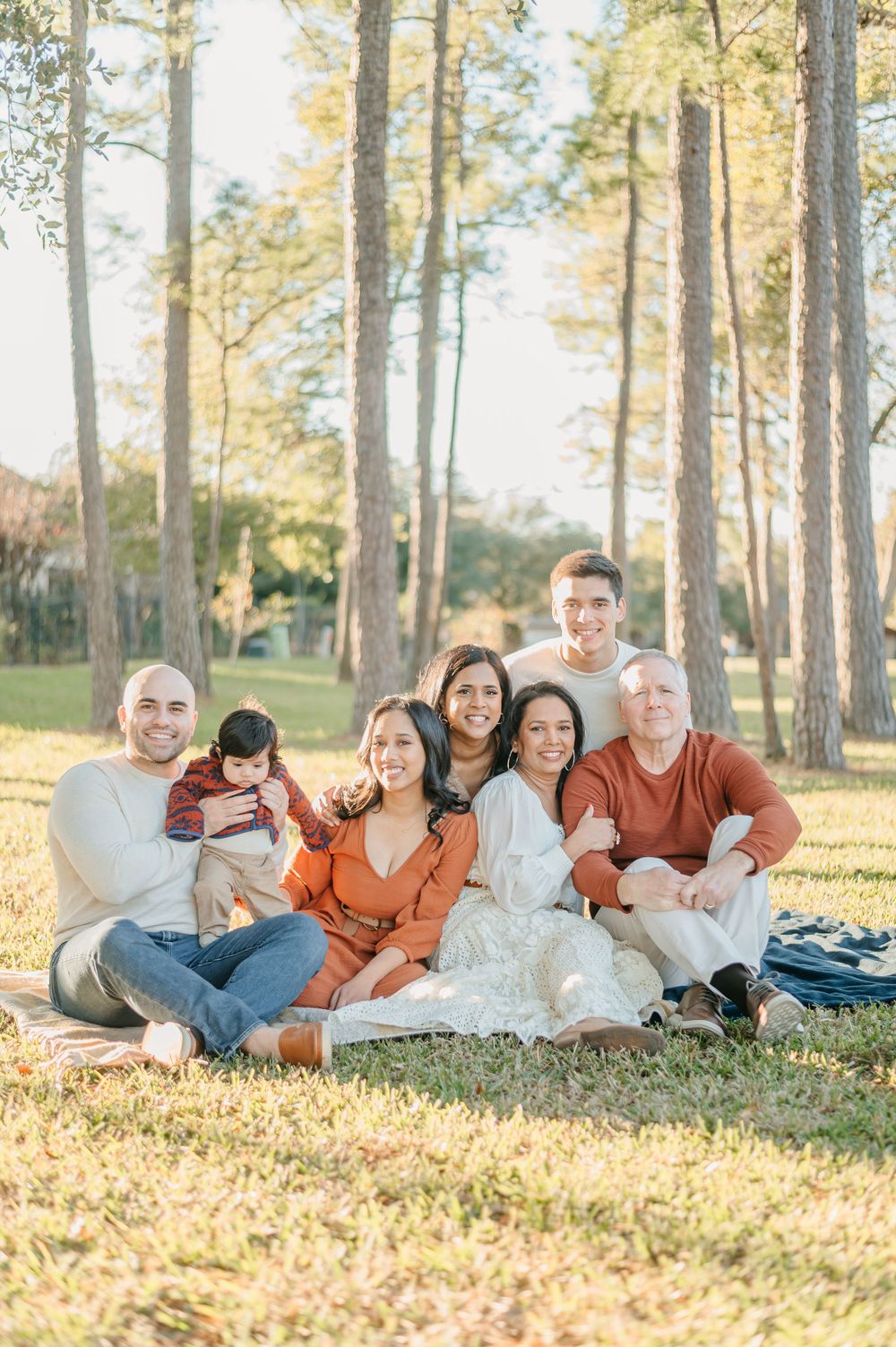 Extended family sitting together on blanket in sunlit pine forest.