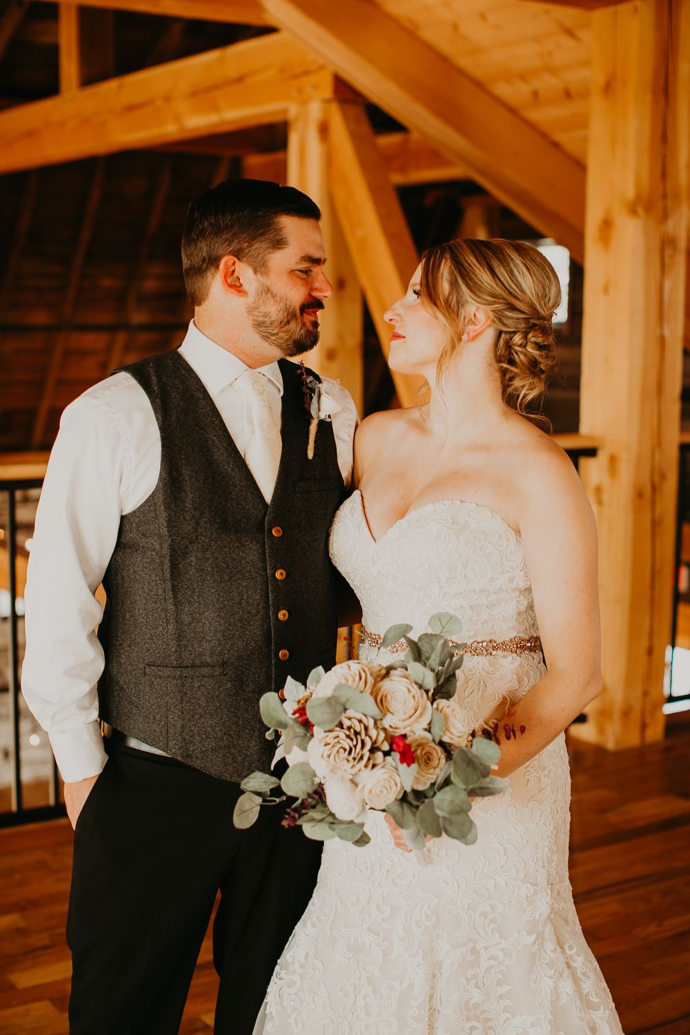 Bride and groom sharing a tender moment in rustic timber barn, bride holding white and pink bouquet.