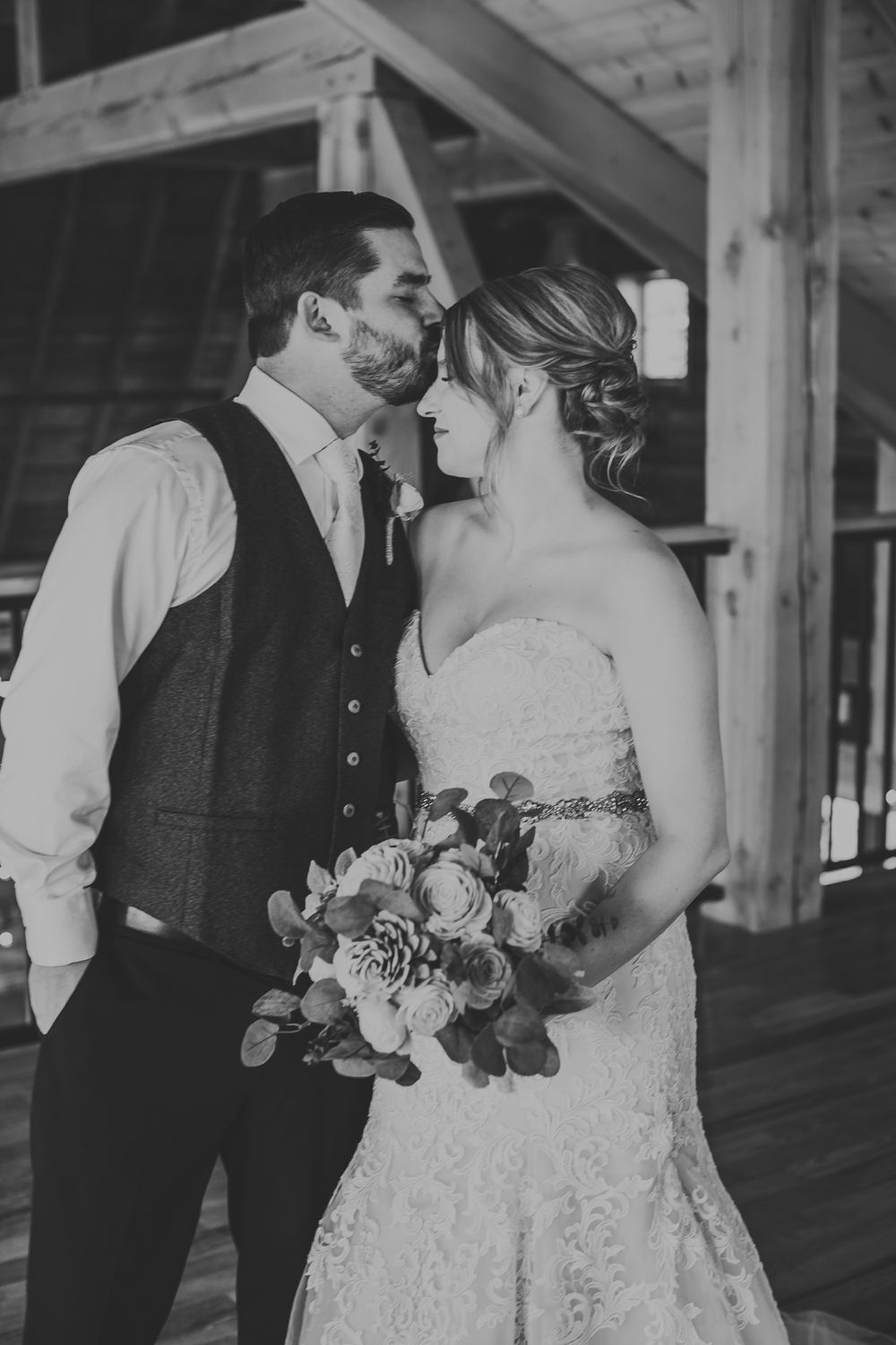 Black and white romantic photo of bride and groom almost kissing in rustic barn wedding venue.