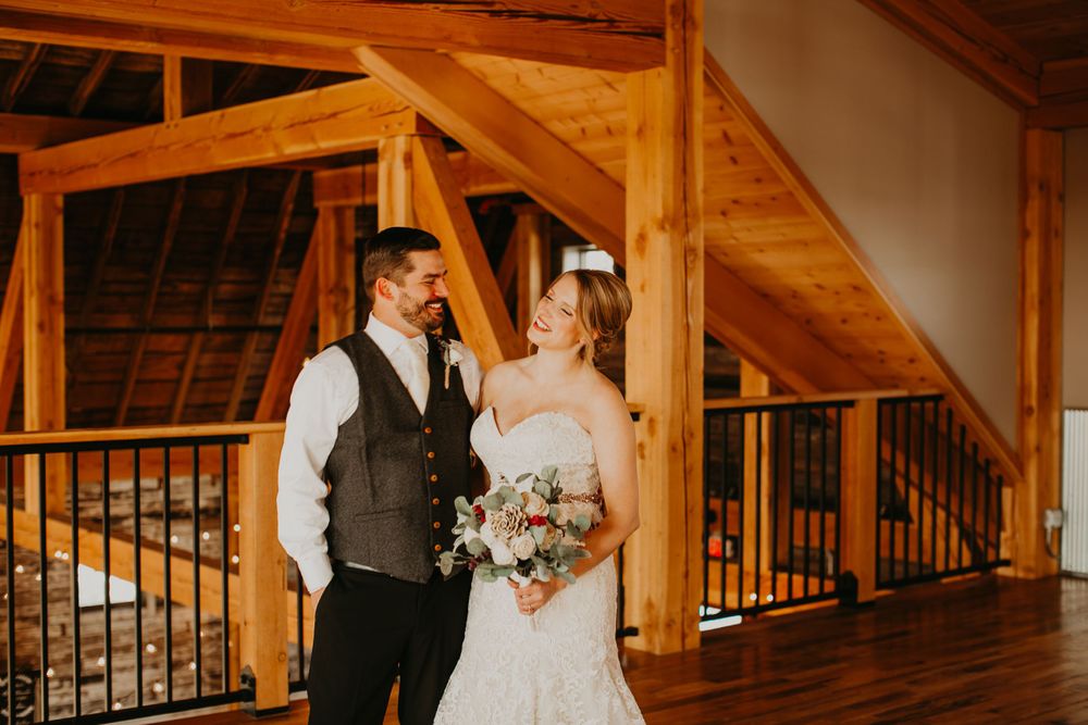 Laughing bride and groom posing together inside elegant timber frame barn wedding venue.