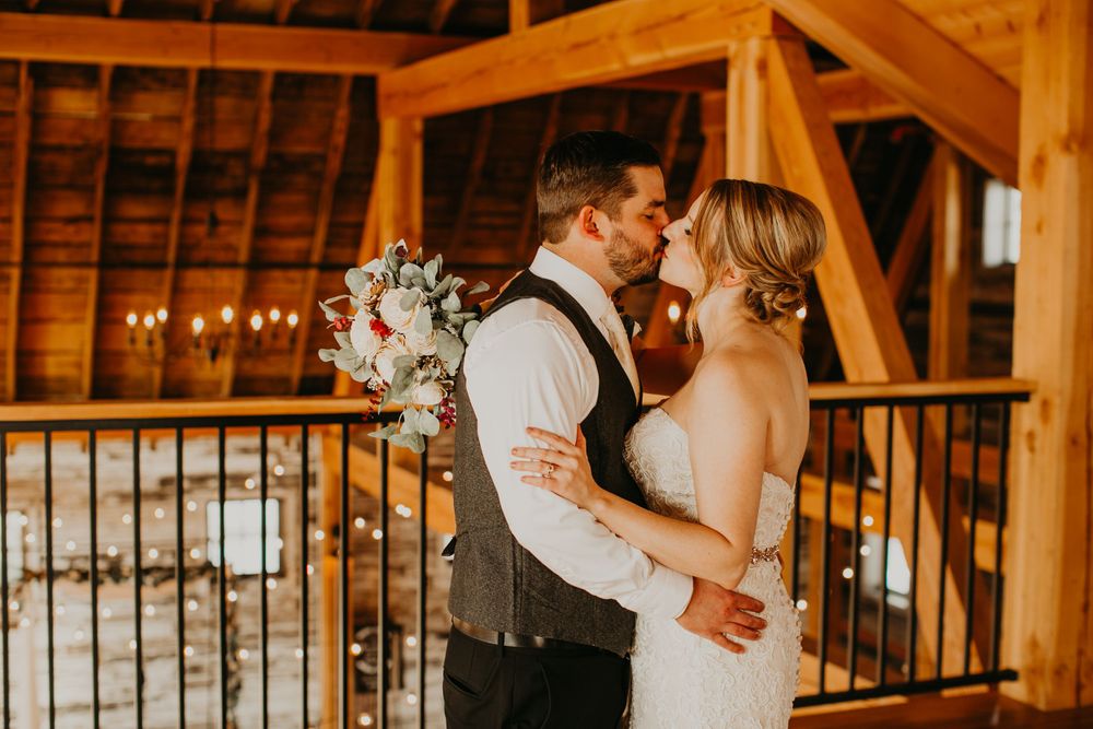 Bride and groom share a romantic kiss in a rustic wooden barn venue on their wedding day.