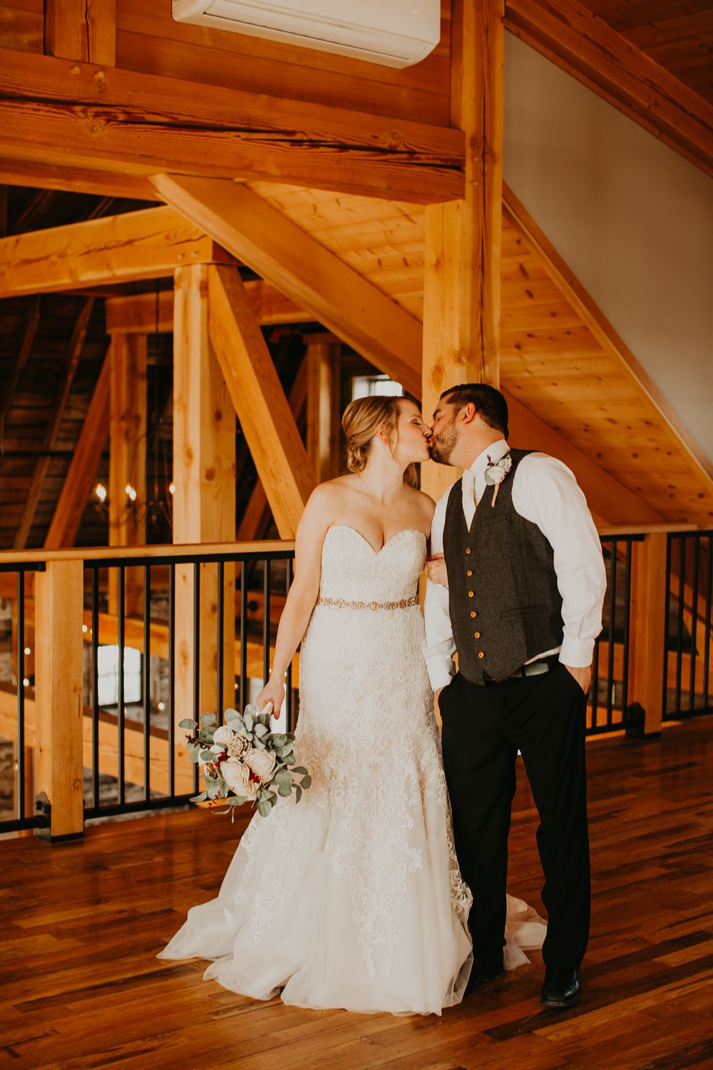 Bride and groom share a kiss on wooden dance floor of a stunning timber frame barn venue.