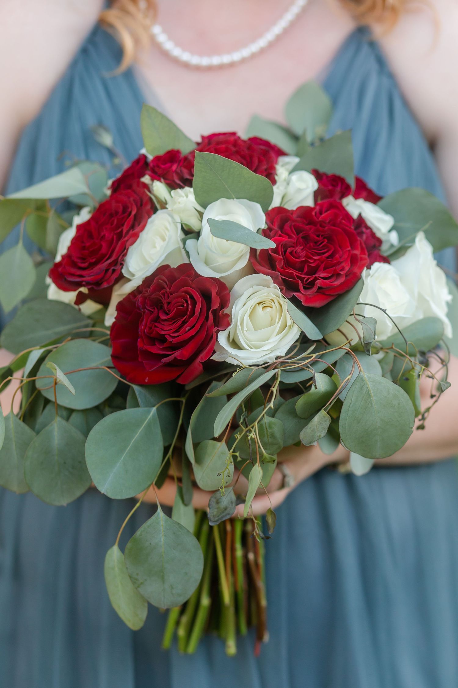 Beautiful bouquet of red and white roses with eucalyptus leaves against dusty blue bridesmaid dress.