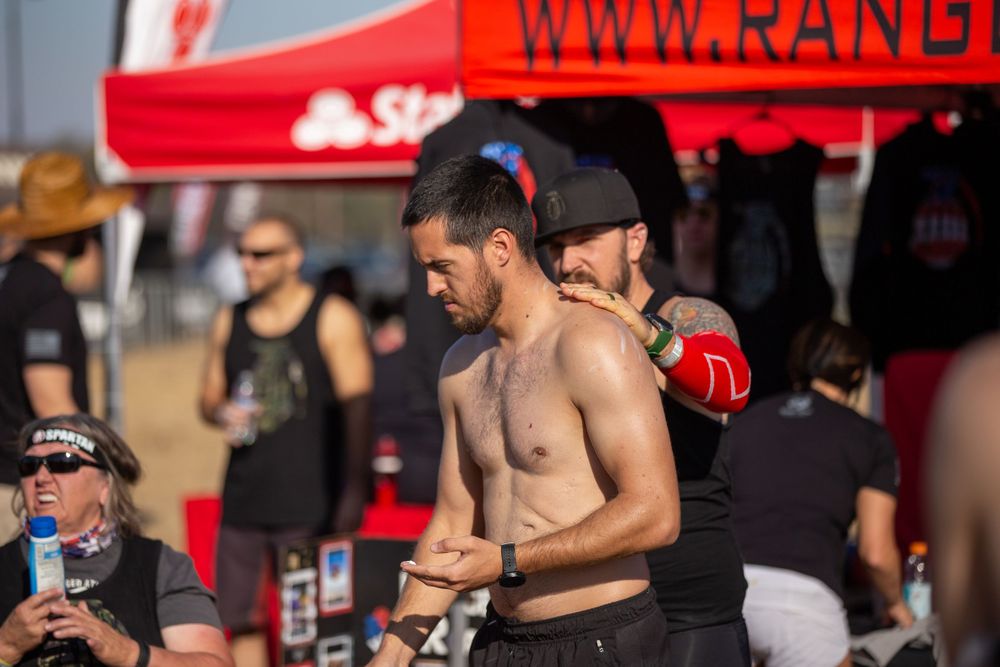 Athletes and spectators gather under red tents at an outdoor sporting competition.