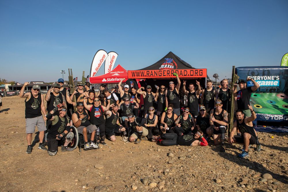 Large group photo of event participants gathered under red promotional tents in a desert setting.