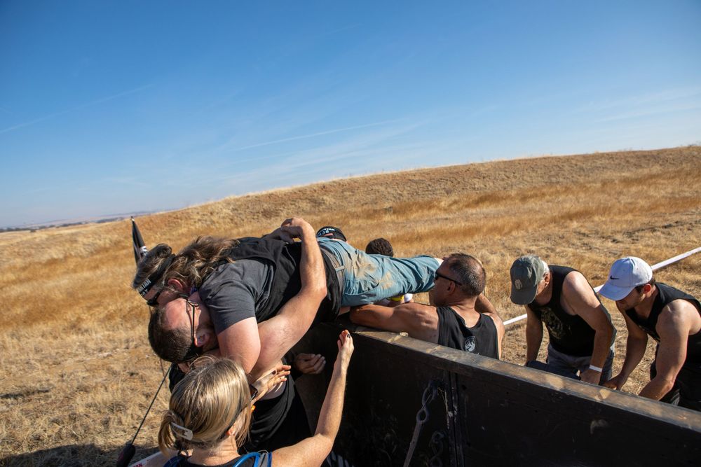 Athletes climbing over obstacle wall during outdoor fitness challenge.