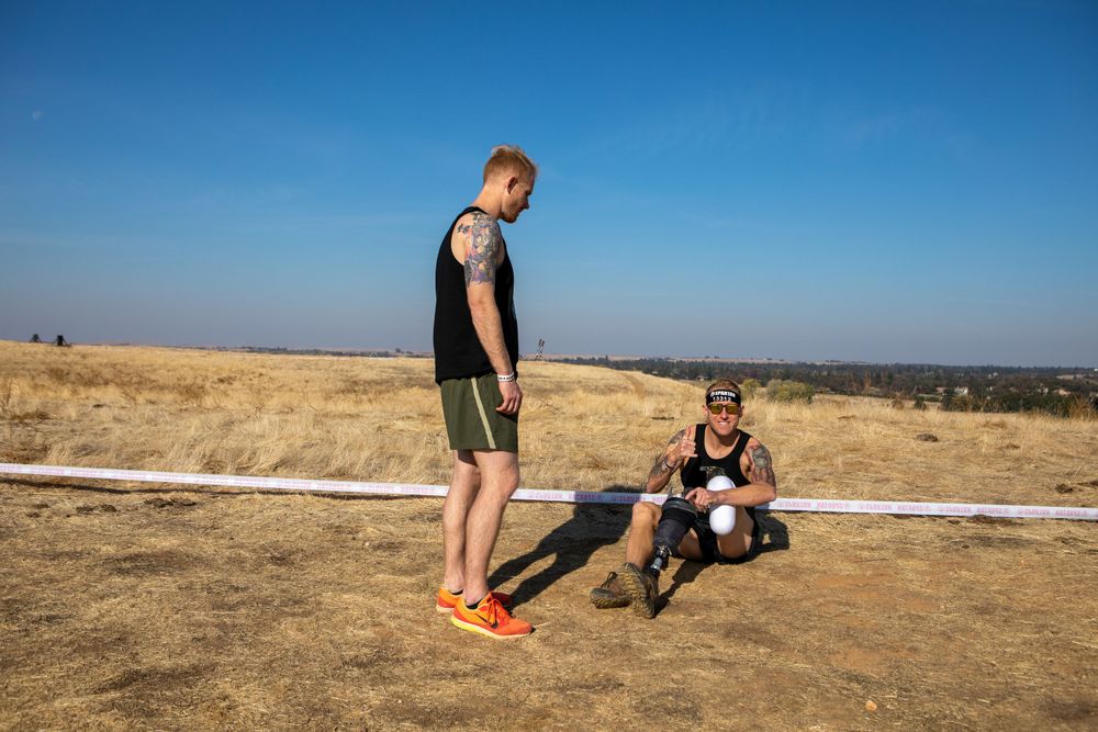 Two participants taking break on dry hillside during obstacle course event.