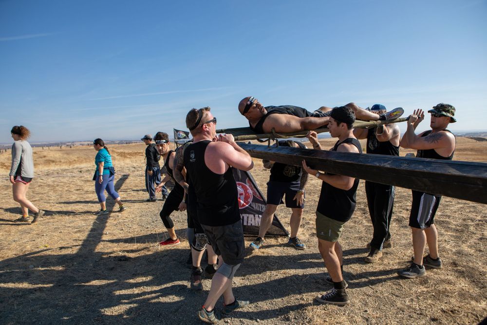 Team working together to carry heavy weight across obstacle course in dry terrain.