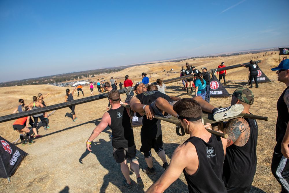 Large group of participants gathered at outdoor obstacle course event station.