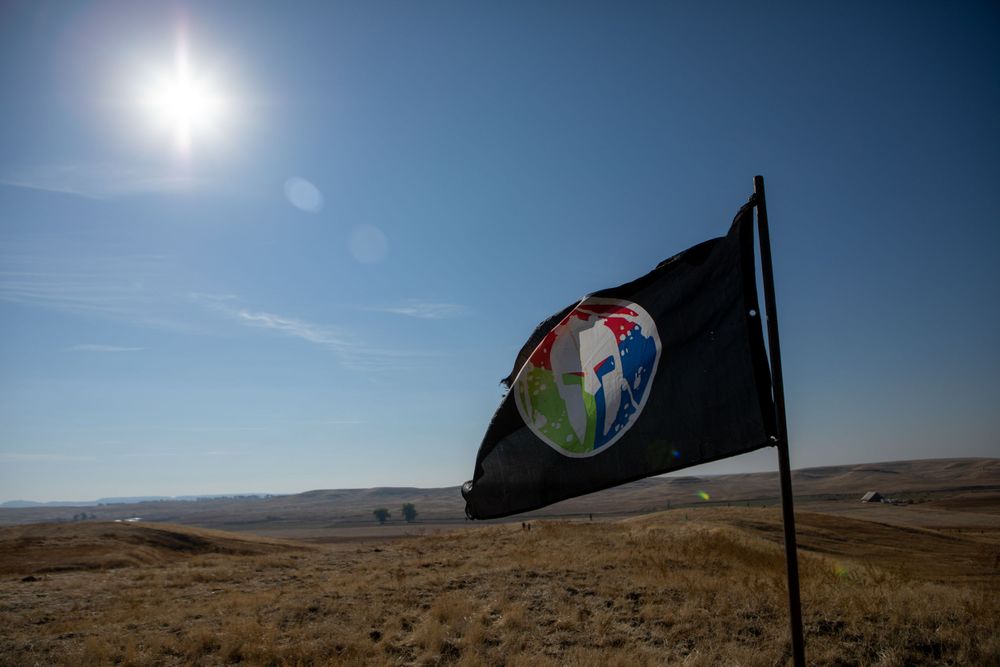 Black flag with logo waving against bright blue sky and desert landscape.