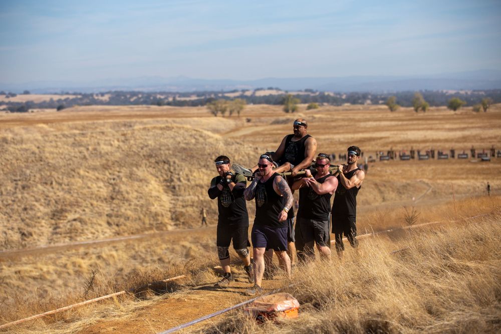 A team works together to carry a participant during an outdoor obstacle course race.