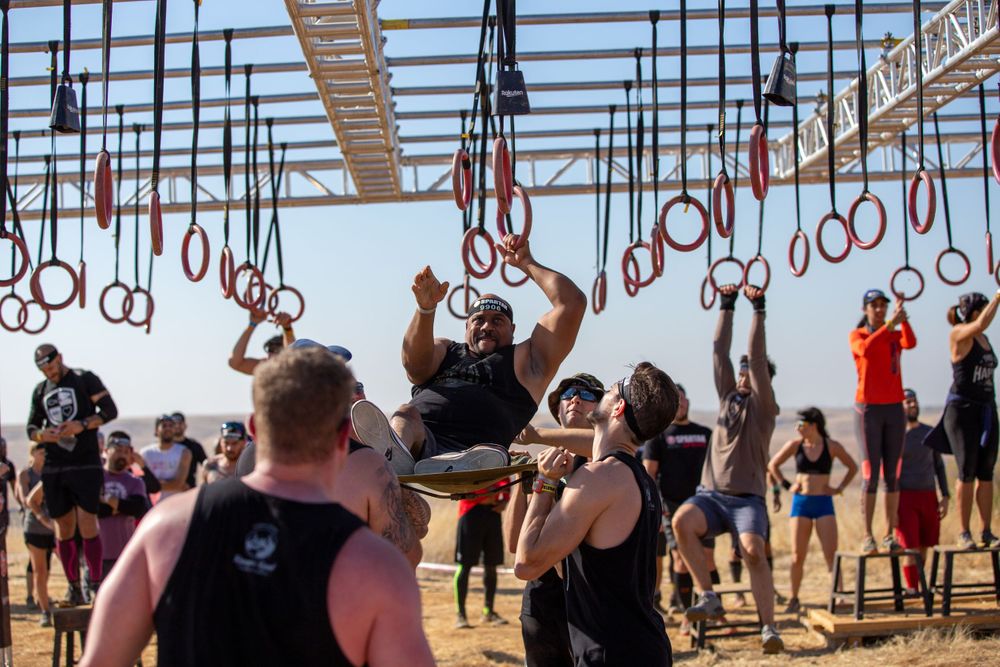 Athletes attempt hanging ring obstacles during an outdoor fitness competition.