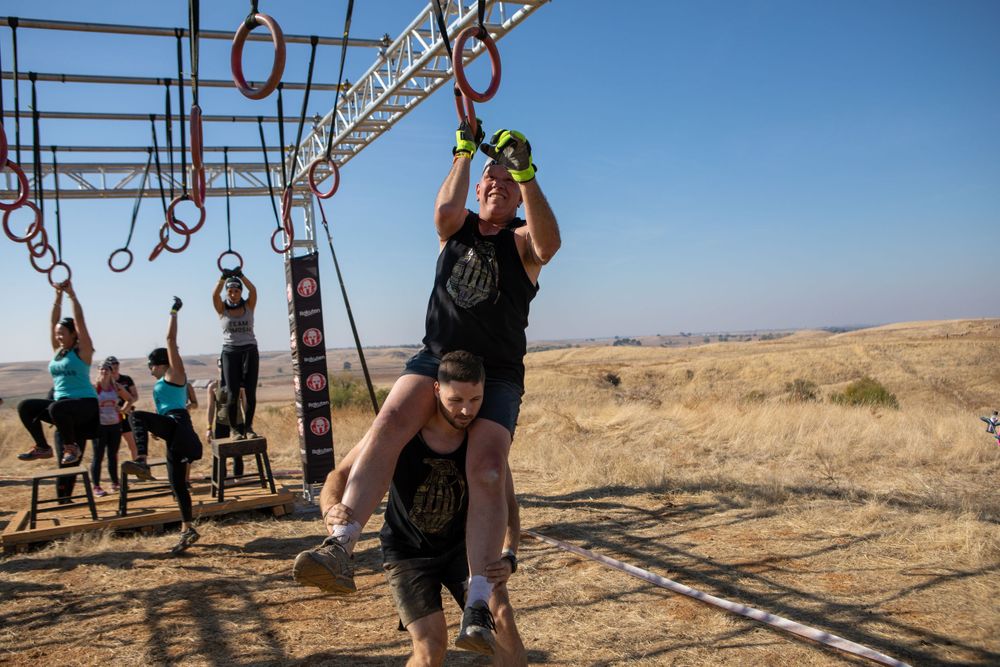 Participant swings from hanging rings in outdoor obstacle course competition.