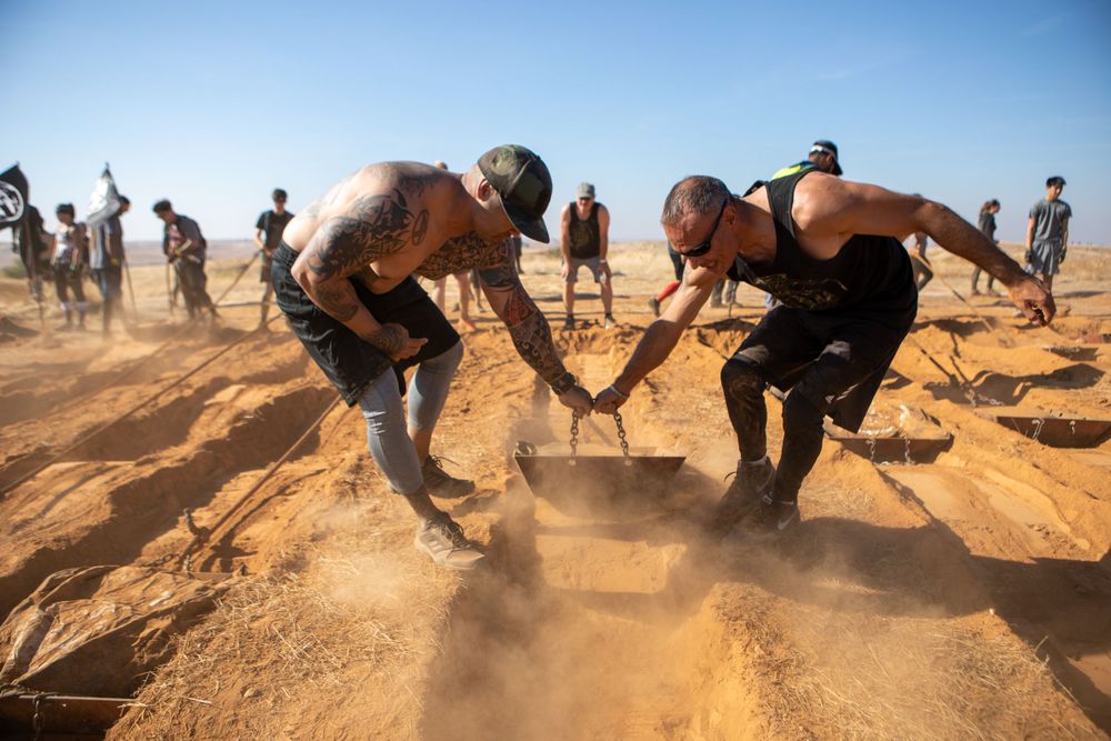 Athletes dig through sandy terrain in intense outdoor obstacle course competition.