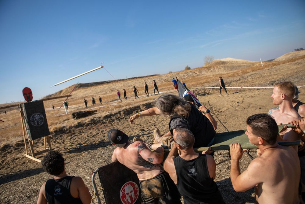 Participants gather at an outdoor obstacle course station in dry terrain.