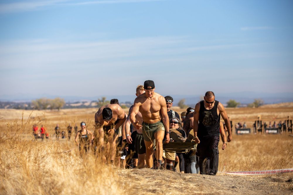 Athletes traverse a challenging trail course through golden dry grass terrain.