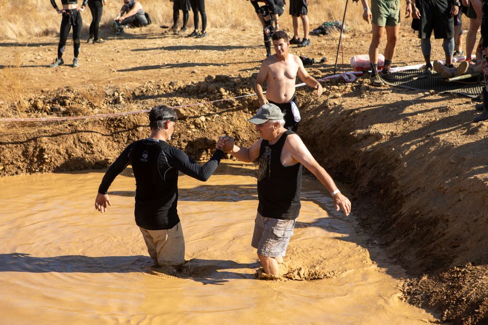 Two participants wade through muddy water during an outdoor obstacle course challenge.