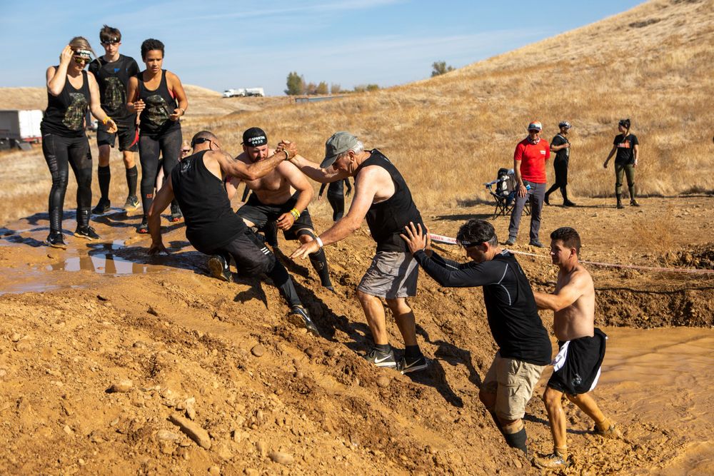 Team members work together to climb up a muddy slope during an obstacle course event.