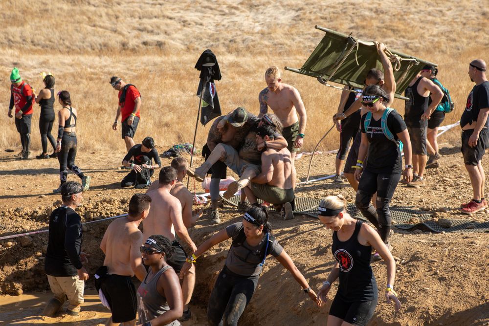 Participants rest and regroup at a checkpoint during a rugged outdoor obstacle course.