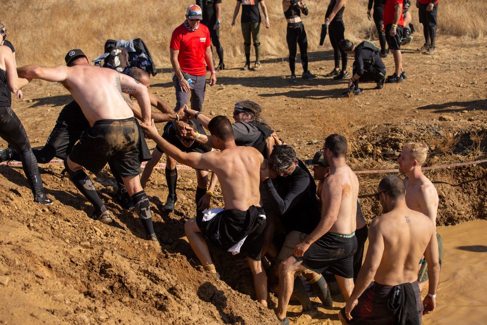 Athletes help each other climb a steep muddy embankment during an obstacle course race.