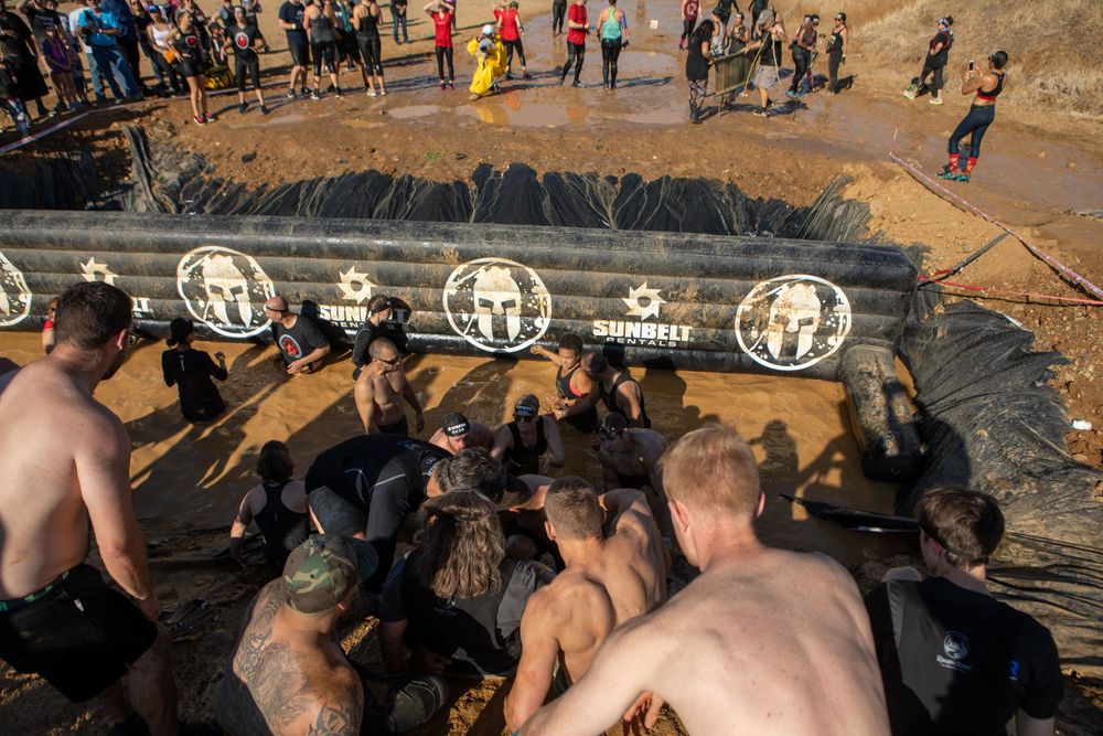 Participants tackle a challenging mud pit obstacle during an outdoor event.