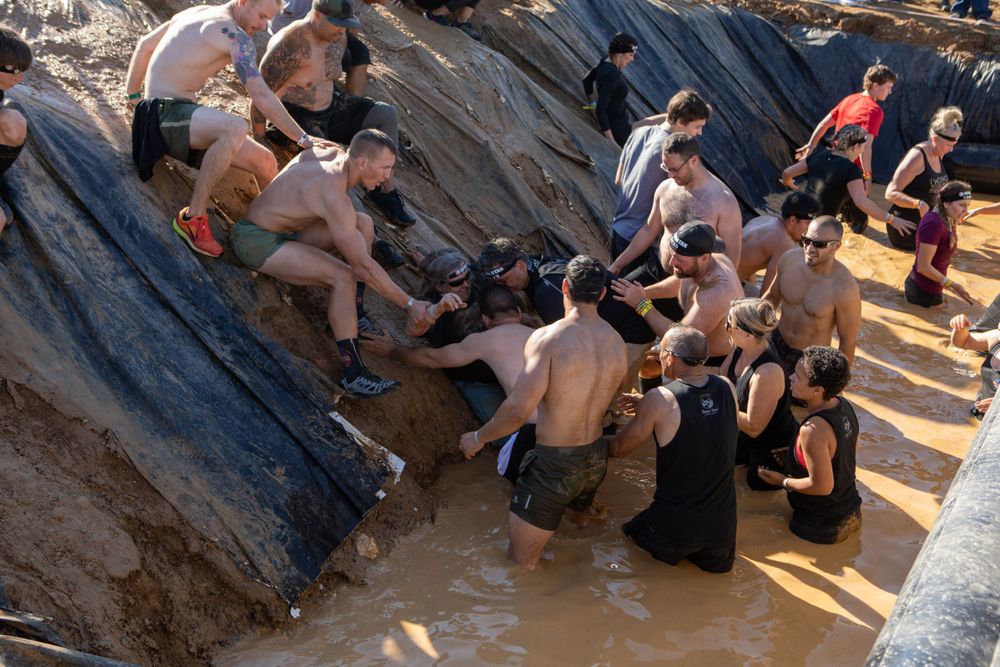 Athletes navigate through a muddy water obstacle during an outdoor challenge course.