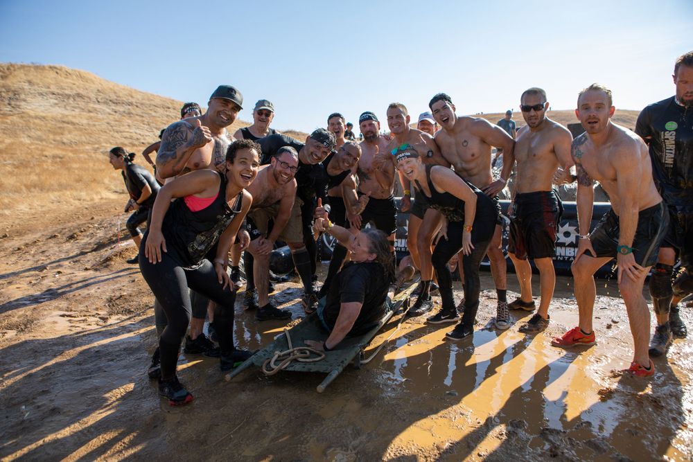 Group of athletic competitors posing together on rocky terrain during a desert obstacle race event.