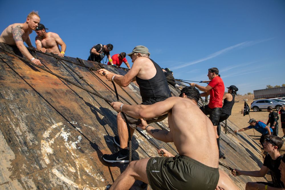 Athletes climbing up a steep rock face during an outdoor obstacle course competition.