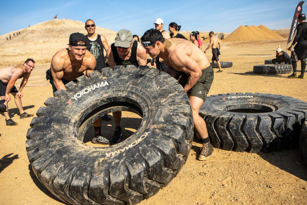 Athletes work together to lift a large tire during an outdoor obstacle course challenge.