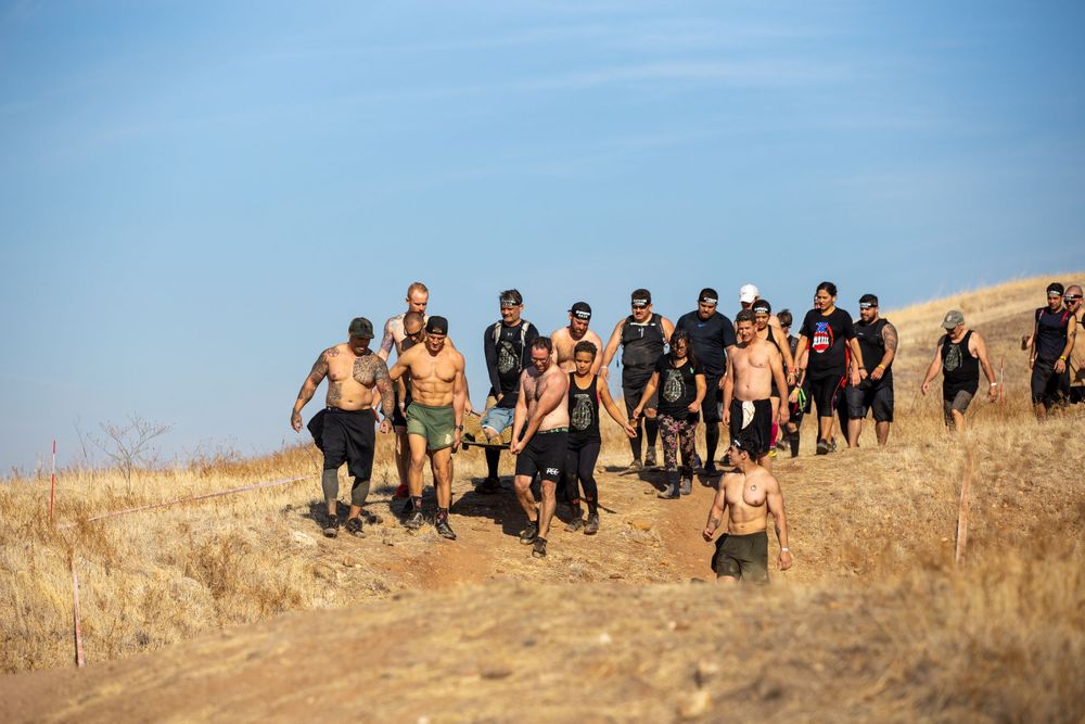 A group of participants climbing up a dusty hill during an outdoor obstacle course event.