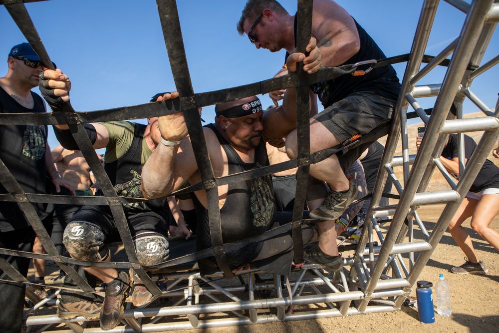 Athletes working together to navigate a metal obstacle course structure under blue skies.
