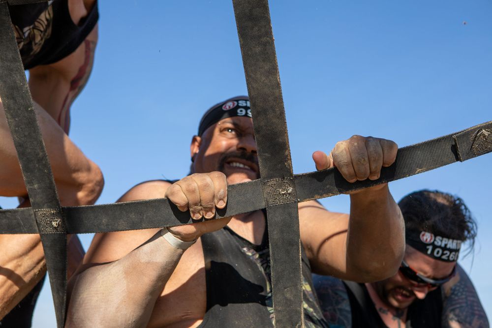 Participants climbing through metal bars during an outdoor obstacle course challenge.