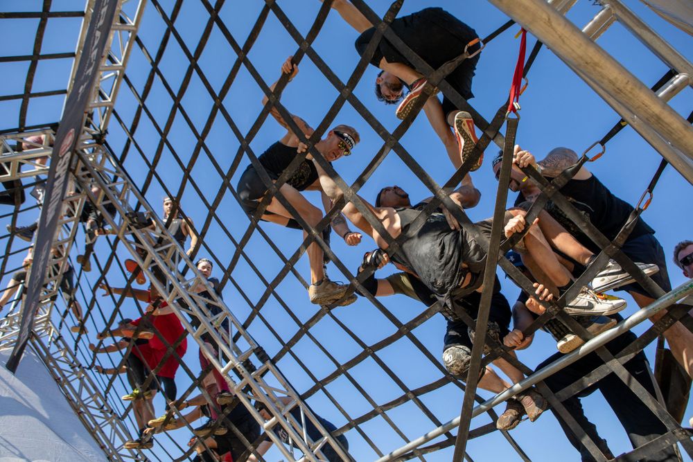 Athletes traversing an overhead metal framework obstacle during an outdoor competition.